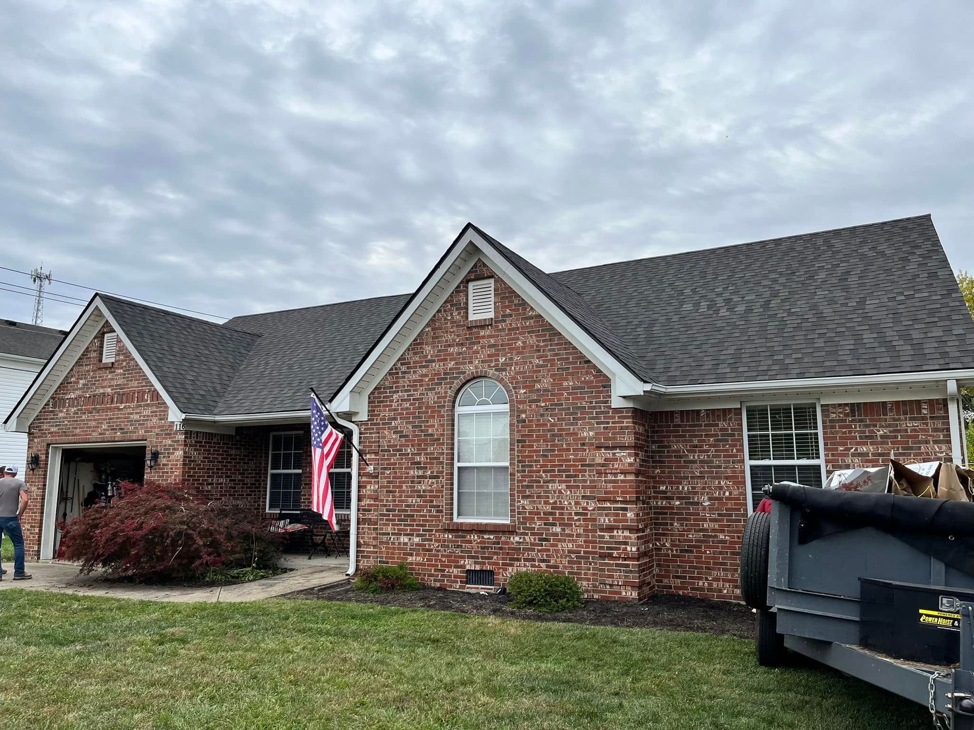 Brick single-story house with a flag by the front porch and a dumpster in the driveway