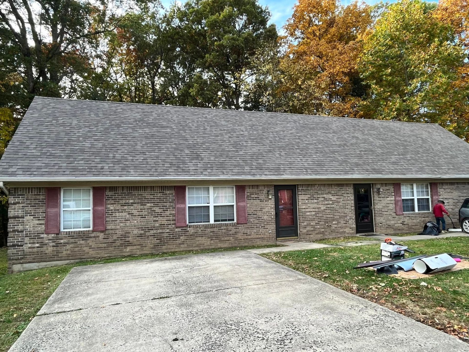 Single-story brick house with gray roof, driveway, and yard debris after storm damage