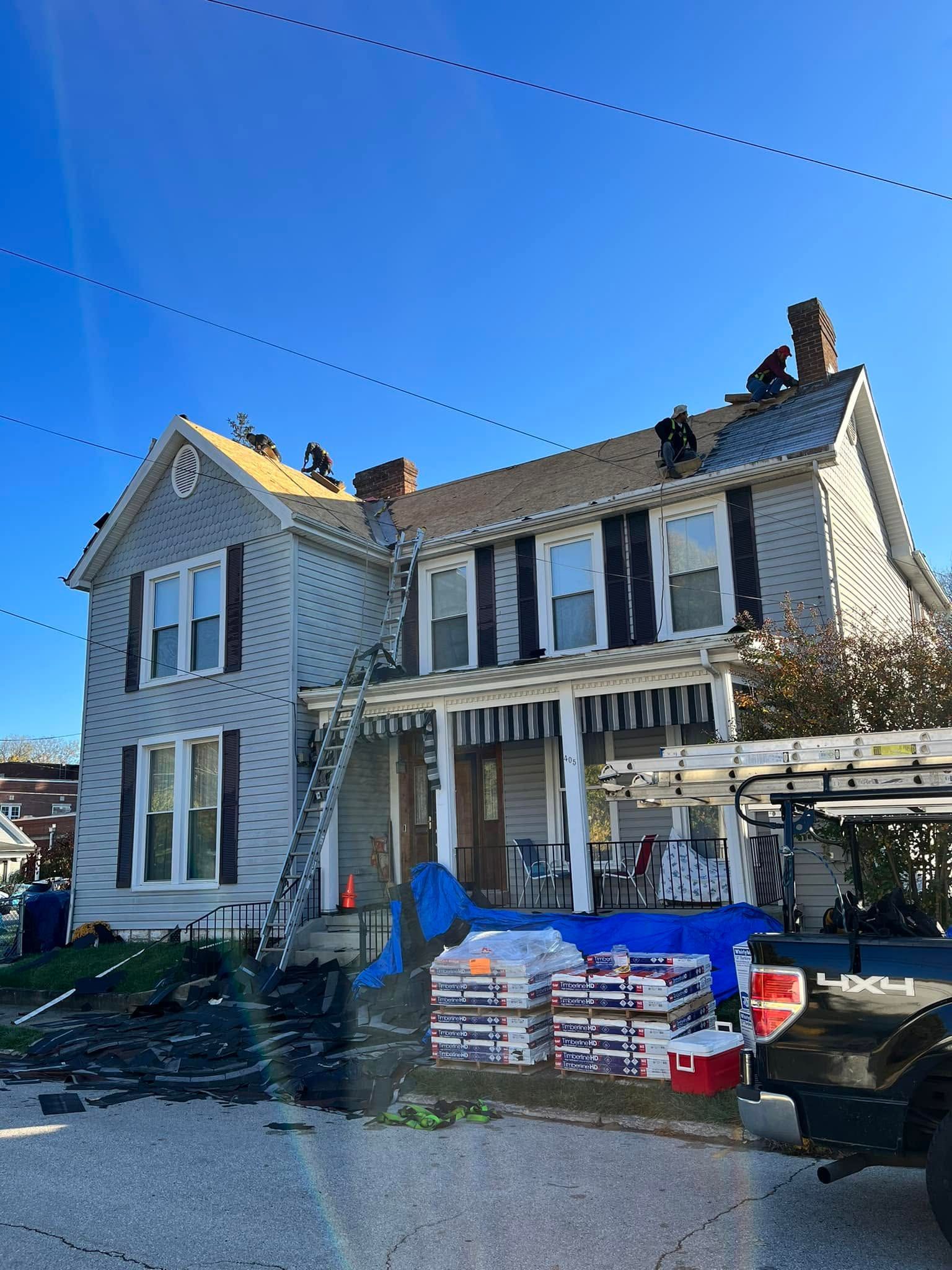 Victorian house with damaged roof, debris and supplies stacked outside under a clear blue sky