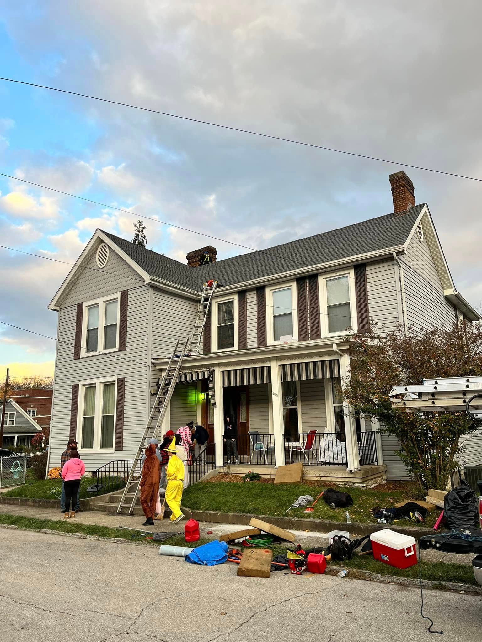 Large gray house with porch decorated for Halloween, with pumpkins and costumed people outside