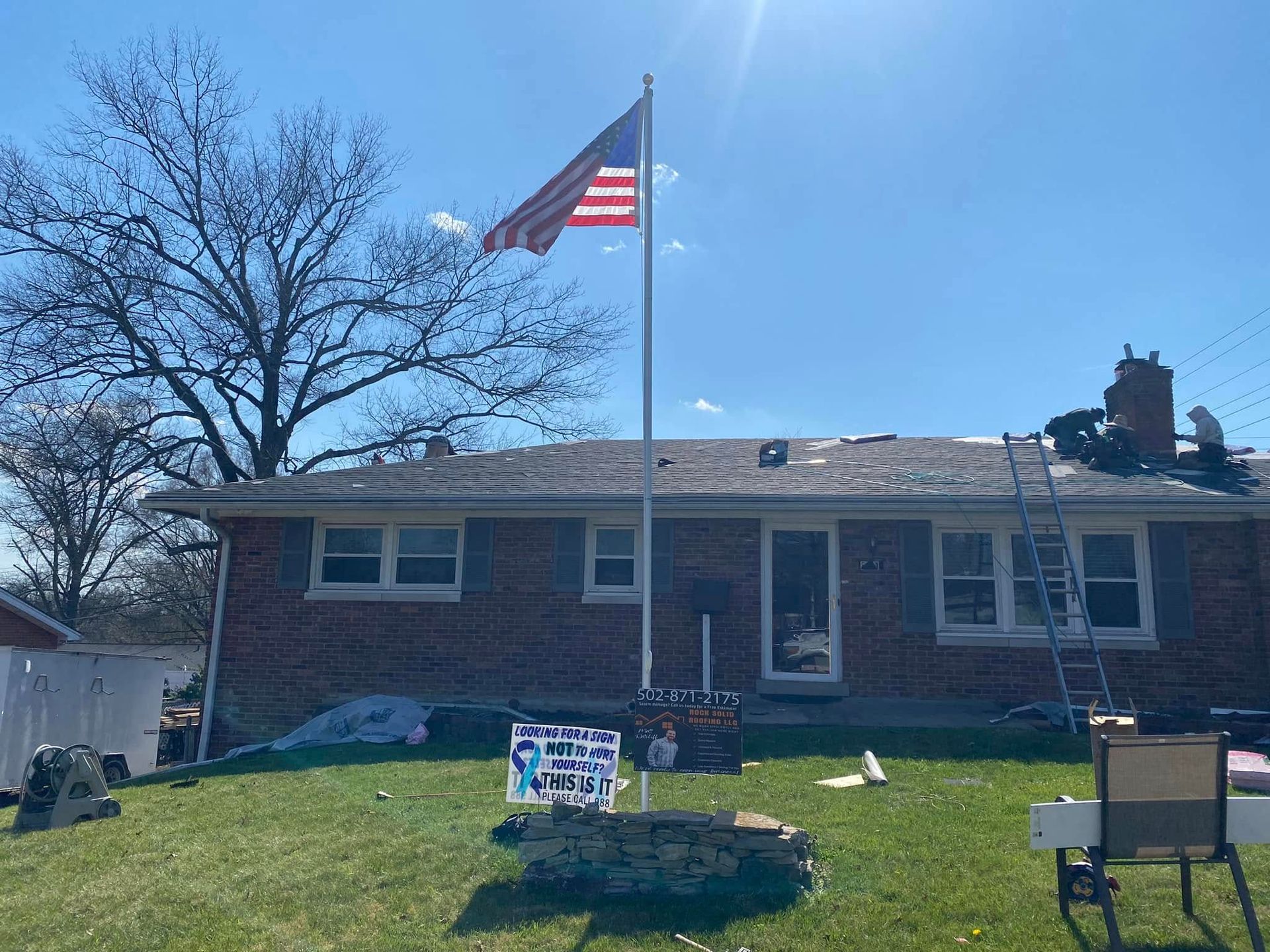 Single-story brick house with an American flag flying in the front yard on a sunny day