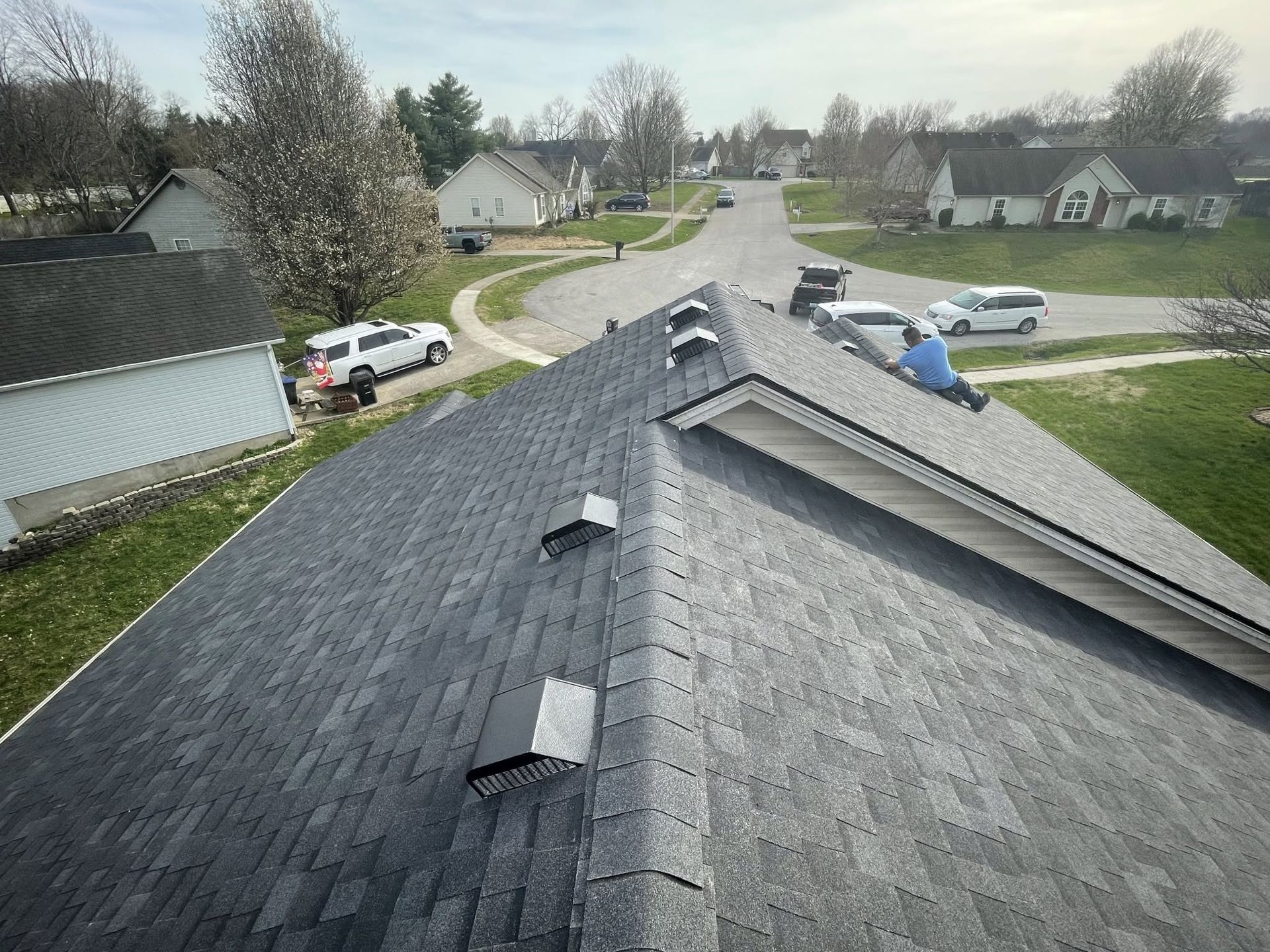 View from a roof with dark shingles overlooking a quiet suburban street and homes