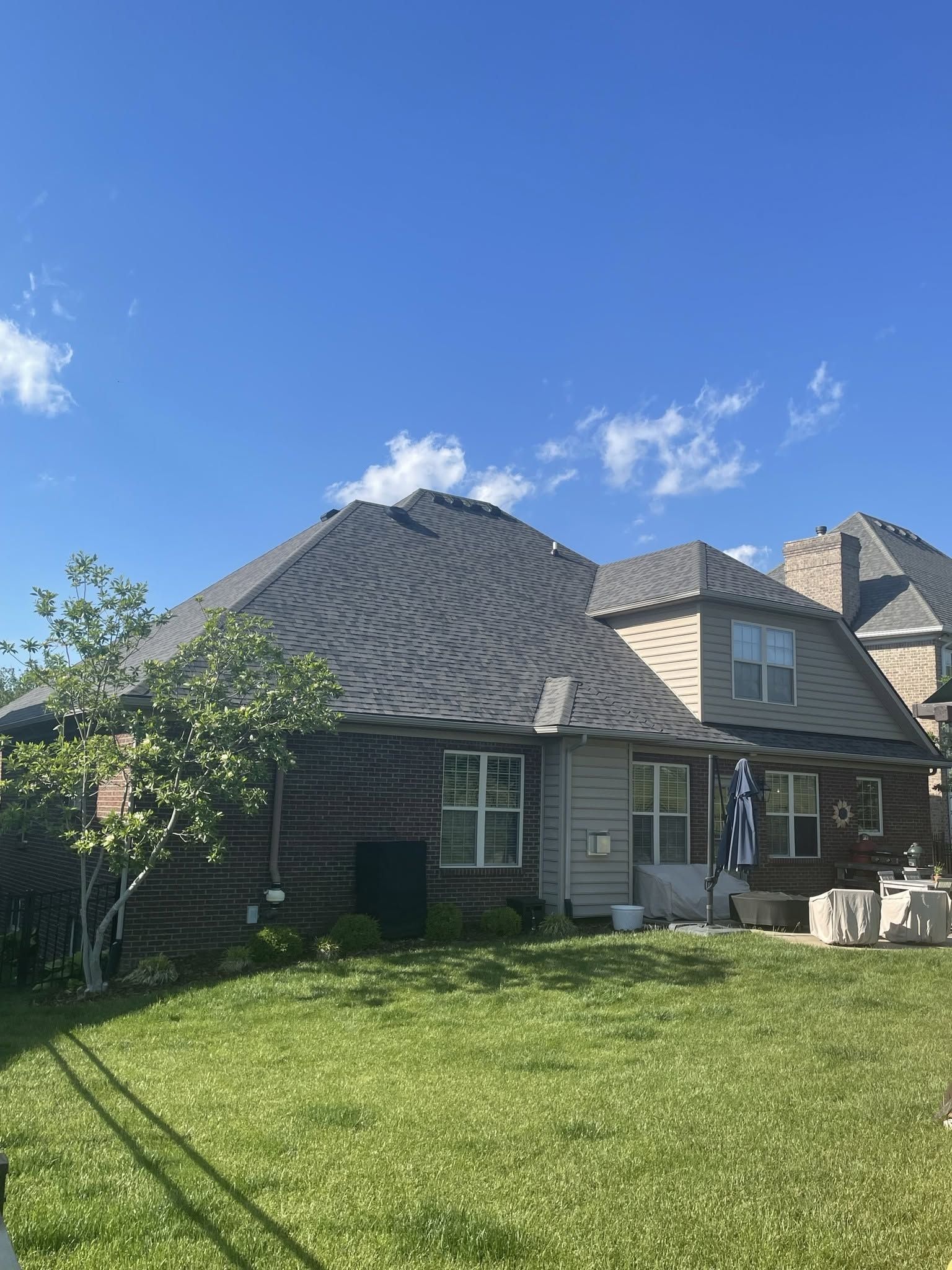Backyard view of a brick house with gray roof, green lawn, and a clear blue sky