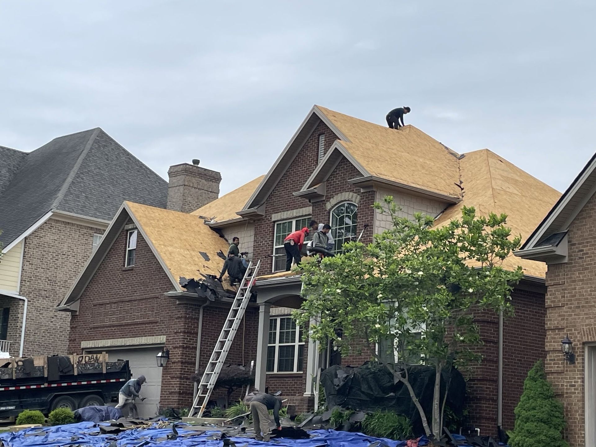 Workers repairing a roof on a brick house, with ladders and construction materials on site