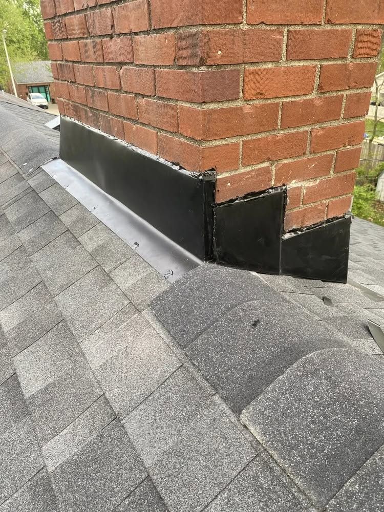Black metal flashing at the base of a brick wall on a gray shingled roof