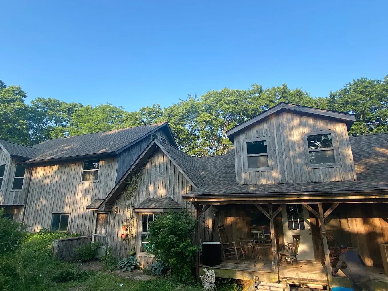 Rustic weathered wooden house with a porch, surrounded by trees under a clear blue sky