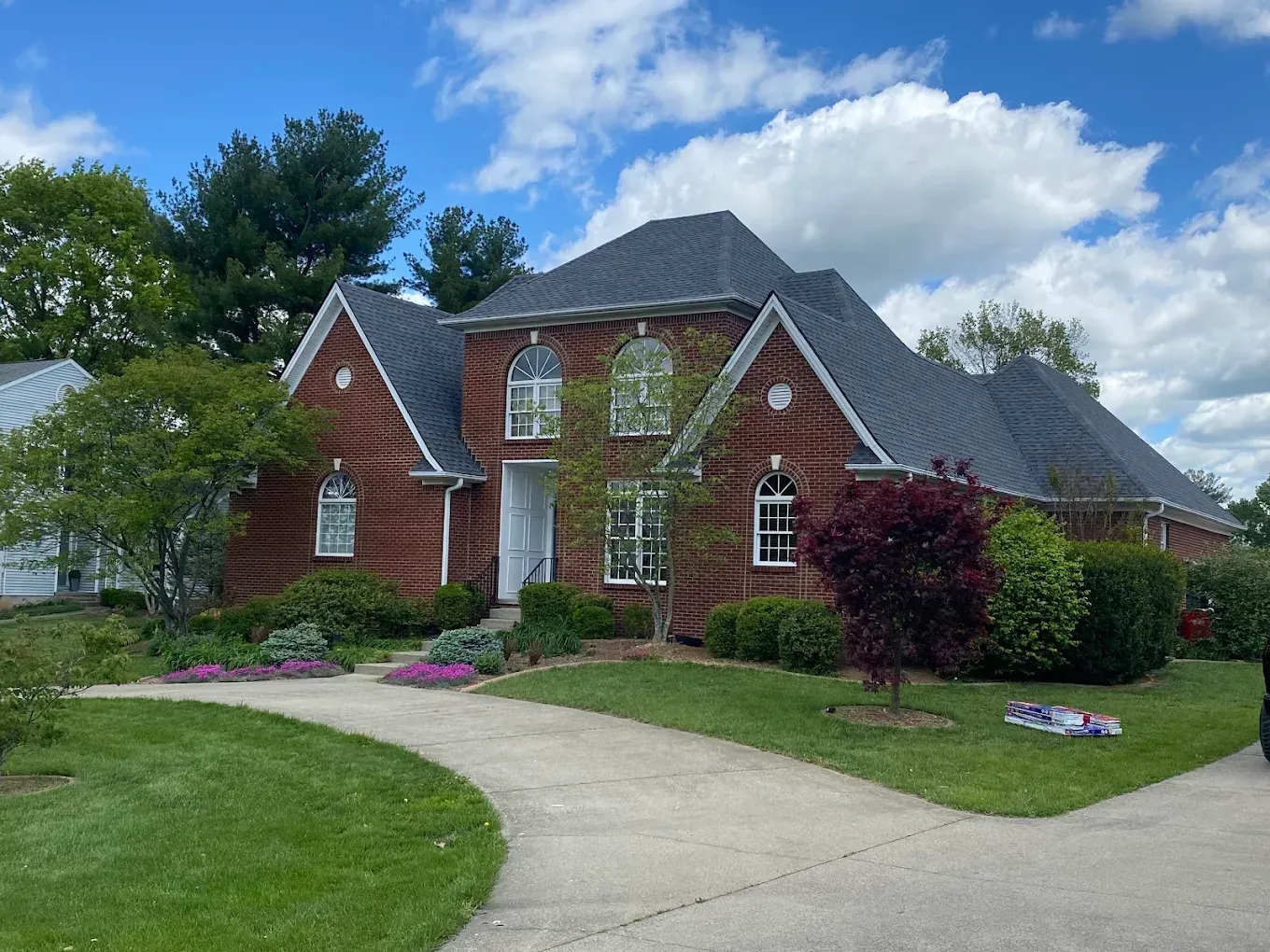 Brick house with a curved driveway, green lawn, and cloudy sky