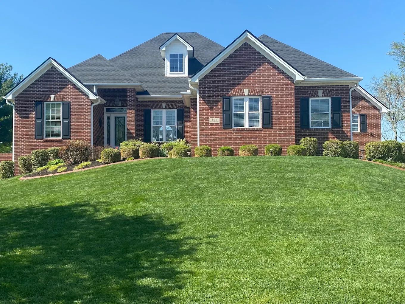 Brick suburban house with dark roof and green lawn under a clear blue sky