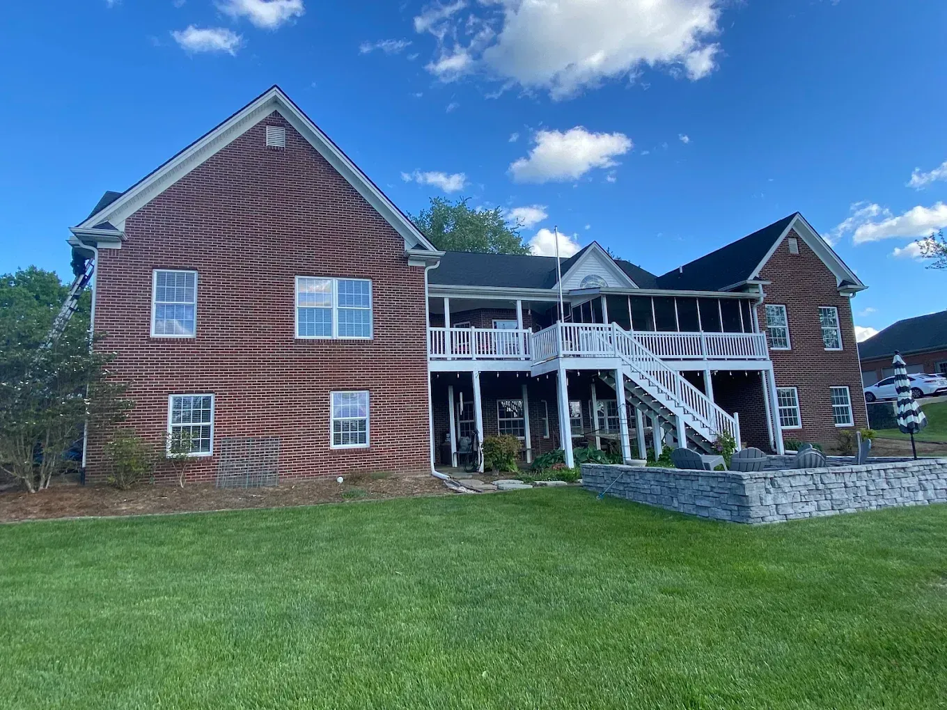 Brick house with white porch and stairs on a grassy lawn under a blue sky