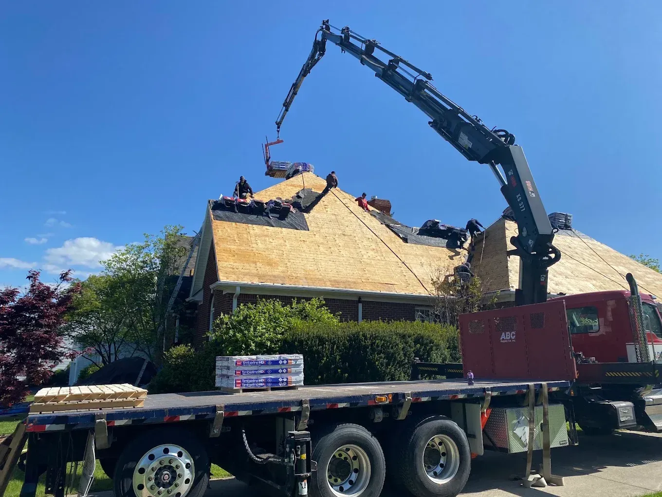 Crane loading debris from a collapsed house roof onto a flatbed truck under a blue sky