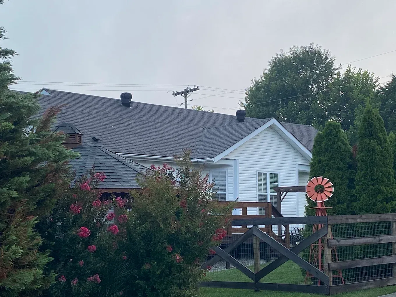 Backyard view of a white house with a wooden deck, pink flowers, and a windmill decoration