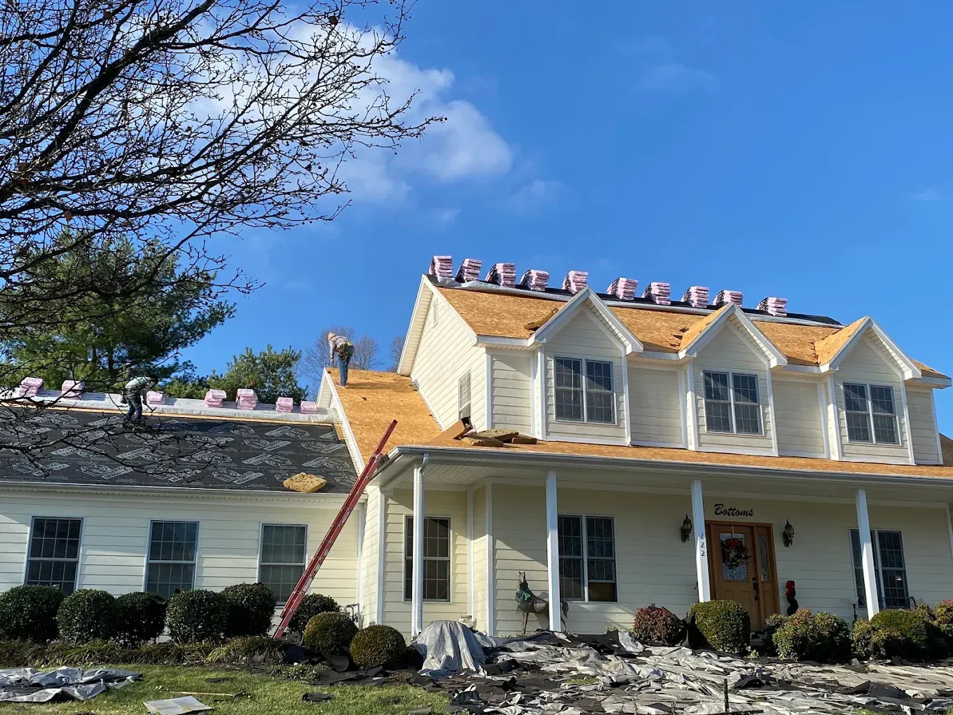 House with yellow roof and porch under a blue sky, with a ladder leaning against it and trees nearby