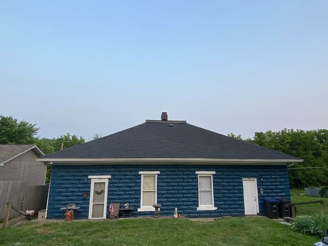 Blue single-story house with a dark roof and white trim, seen from the front under a clear sky