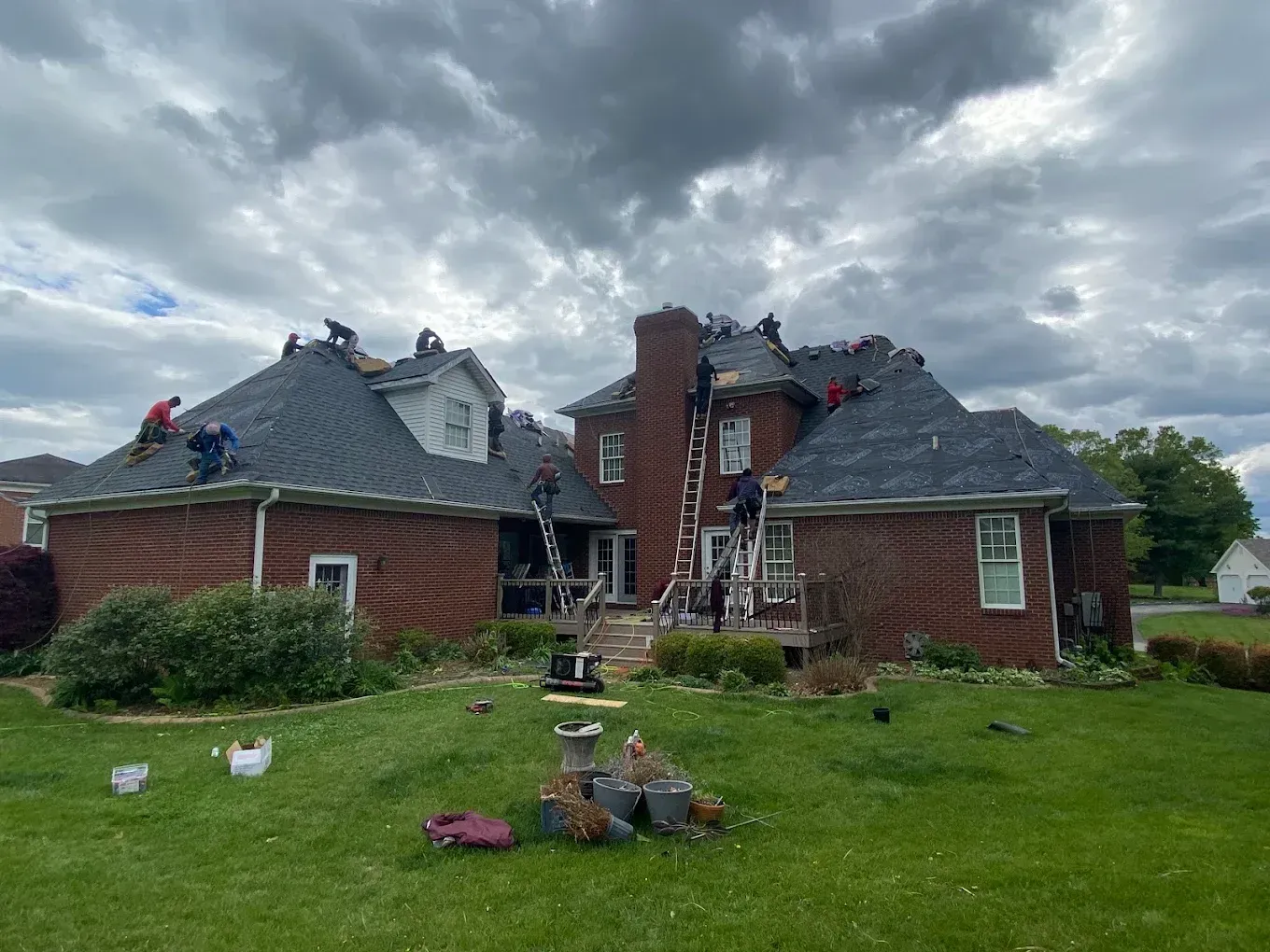Severely damaged brick house with a collapsed roof under a cloudy sky, debris scattered on the lawn