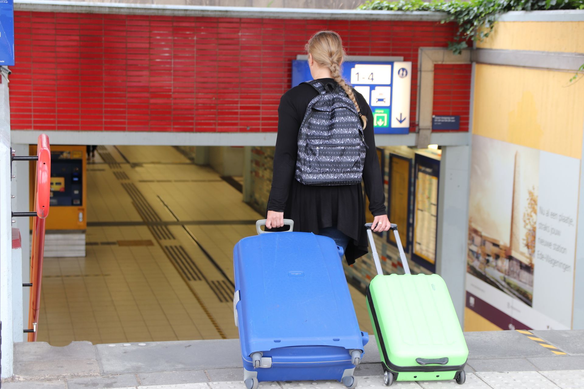 Een persoon die twee koffers naar een roltrap bij de ingang van een metrostation trekt.