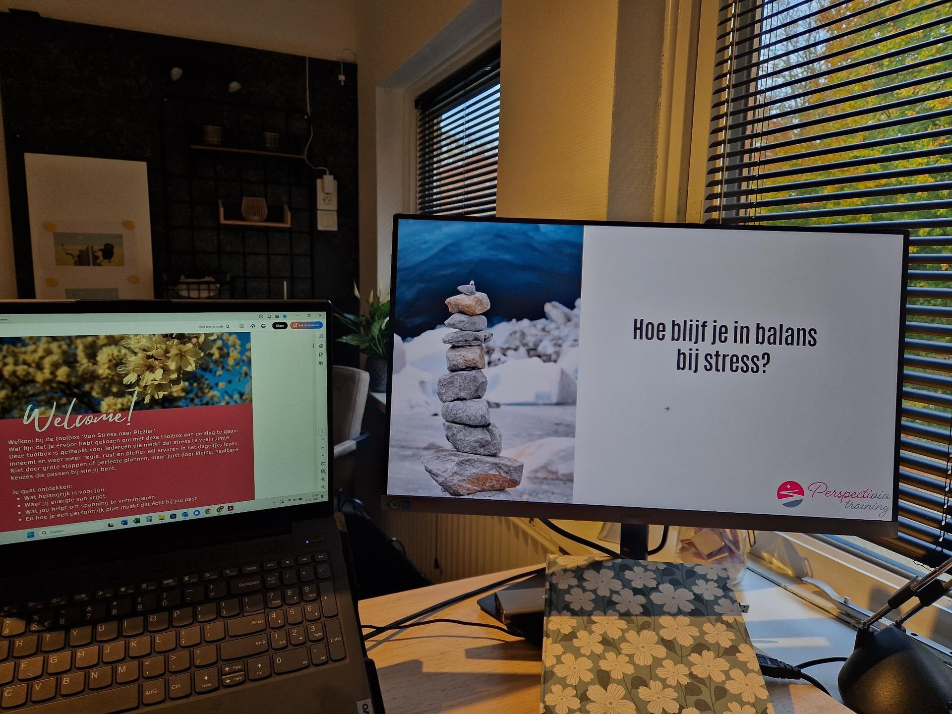 Bureau met laptop en monitor waarop een reclame voor een stapel stenen naast een raam te zien is.