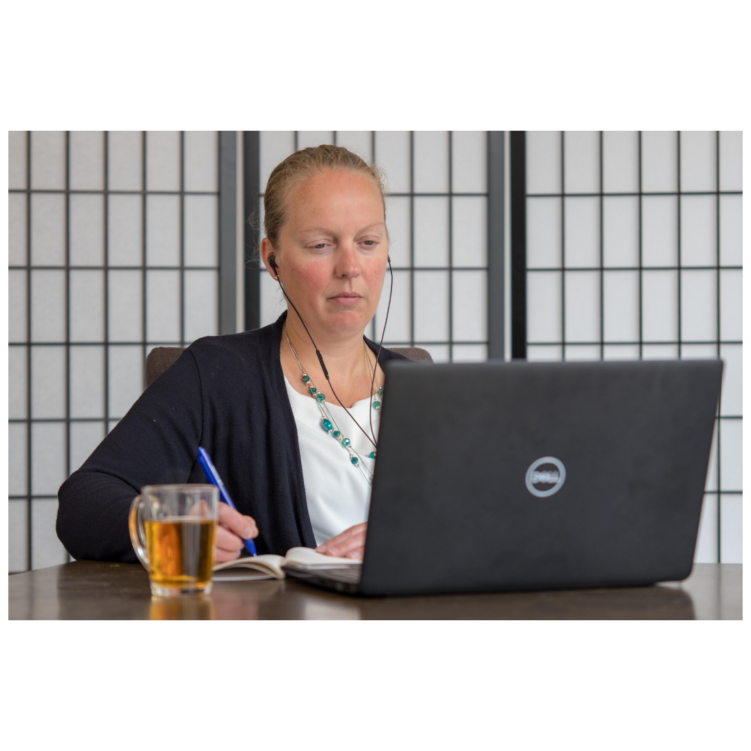 Vrouw werkt aan een laptop aan een tafel met een glas thee en maakt aantekeningen.