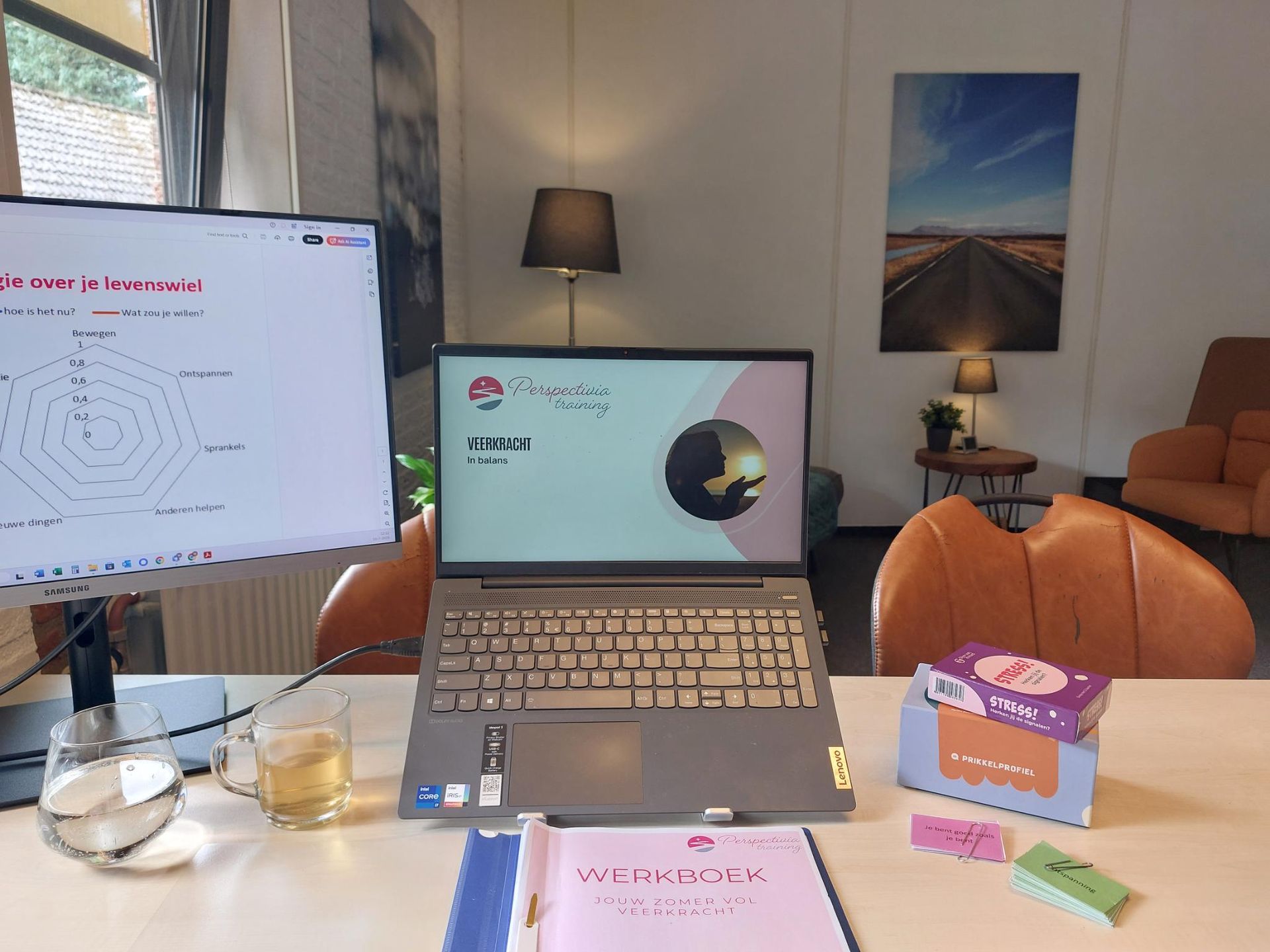 Bureau met laptop en monitor in een lichte kamer, met een lamp, stoel en wat kleine kantoorartikelen op tafel.