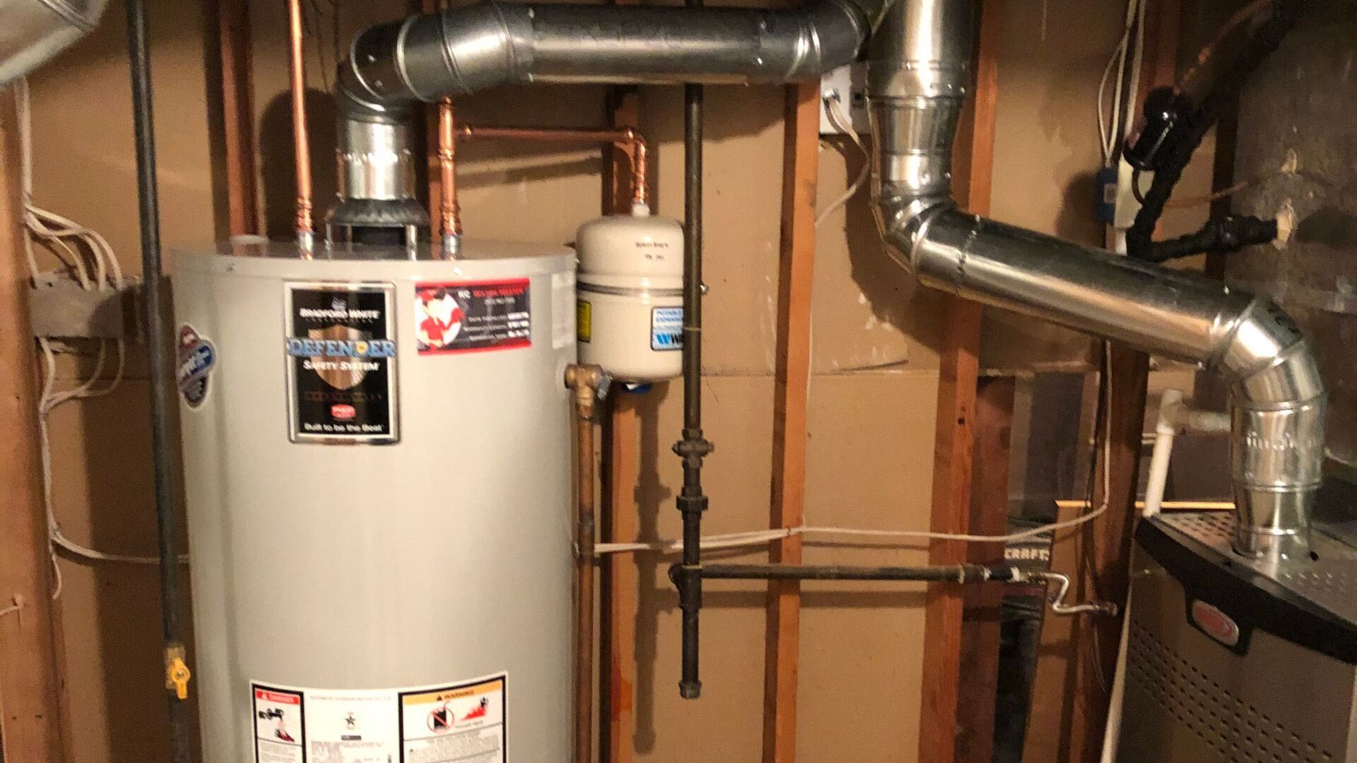 A water heater is sitting in a basement next to a furnace.