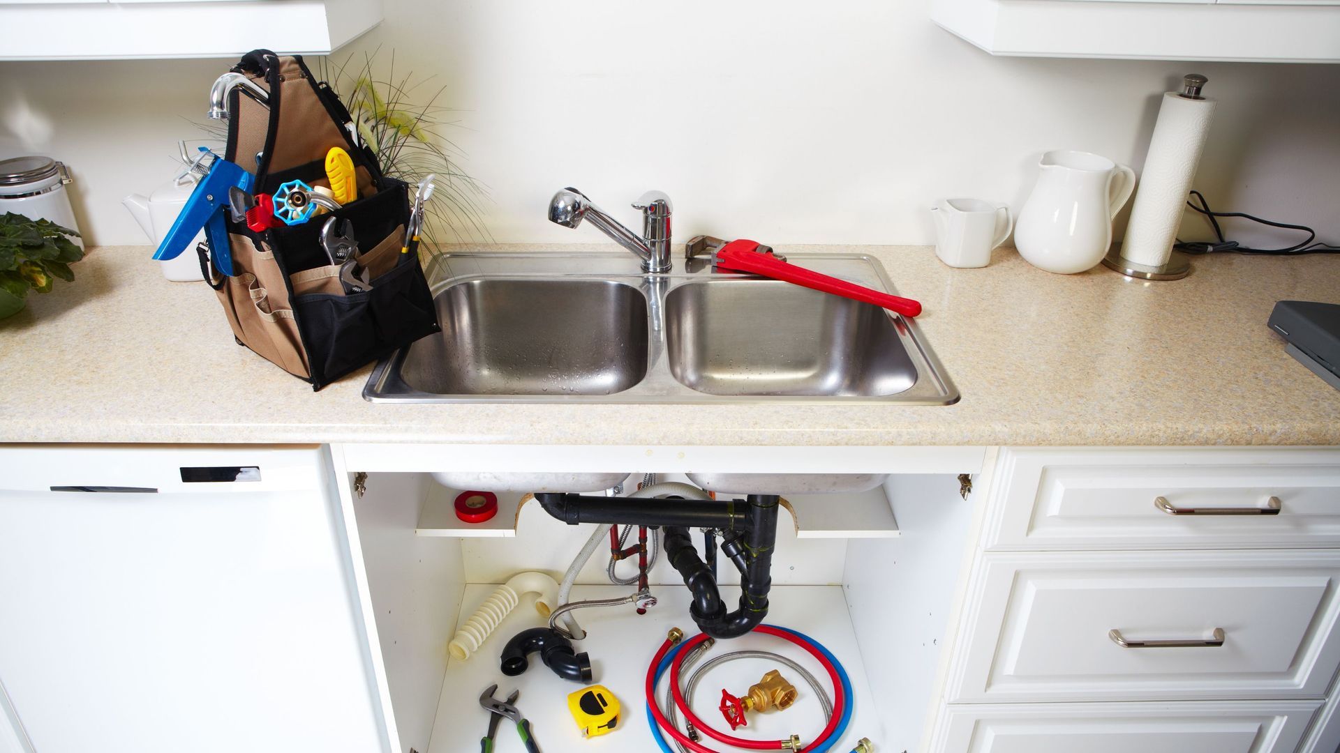A kitchen sink is being repaired by a plumber.