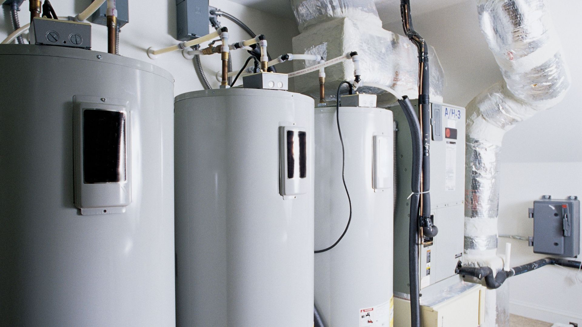 Three water heaters are sitting next to each other in a basement.