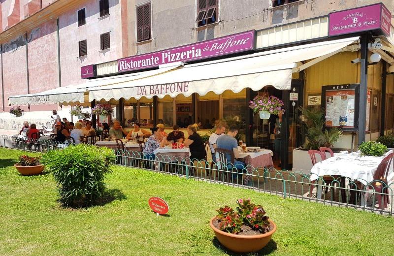 Terrazza esterna del caffè con tavolini all'aperto sotto una tenda a righe, accanto a un piccolo giardino erboso.