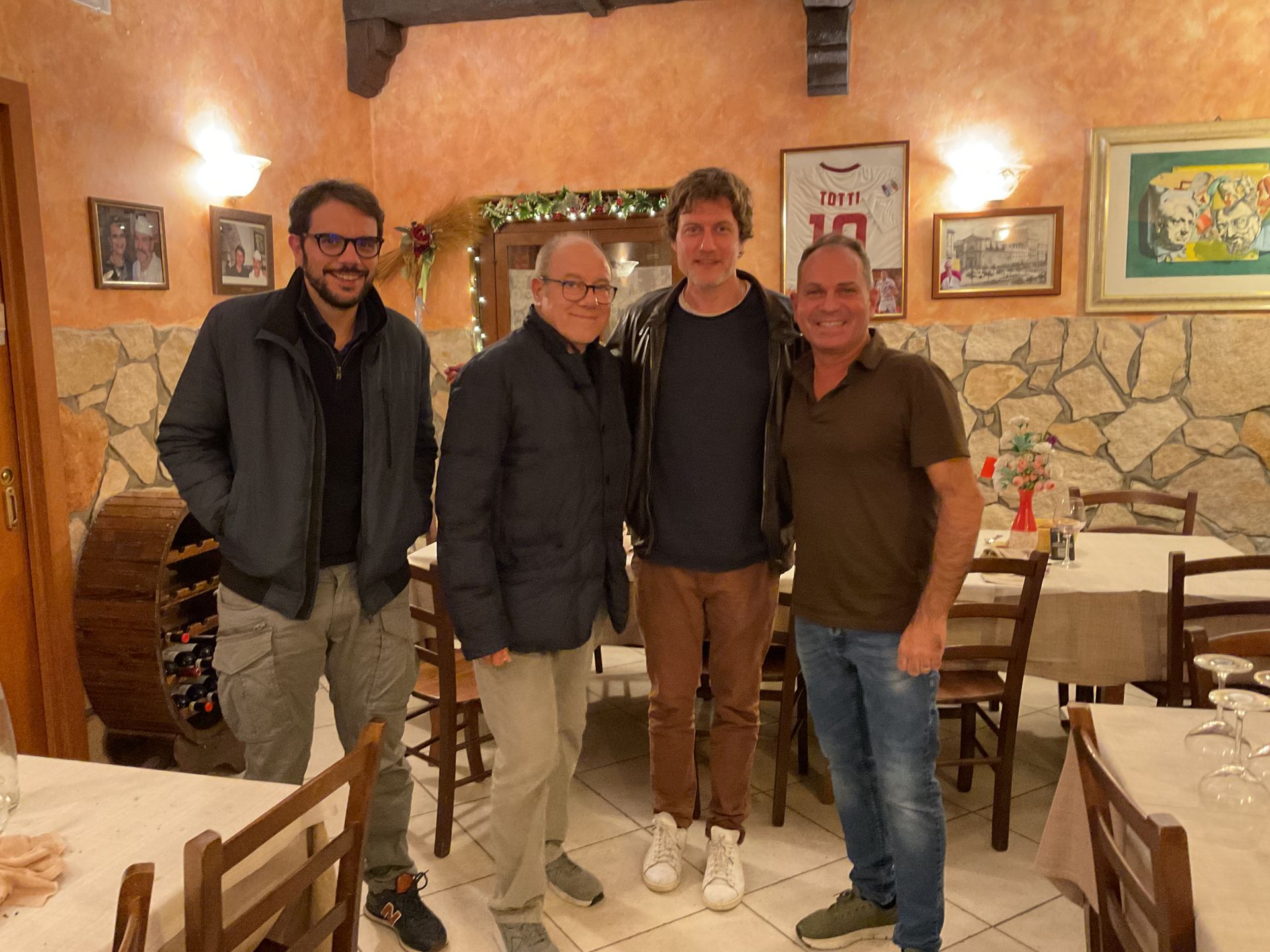 Quattro uomini in piedi insieme in un accogliente ristorante con pareti in pietra e tavoli in legno.