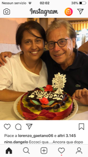 Una coppia sorride al tavolo di un ristorante, ammirando un dessert colorato guarnito con frutta e fiori.