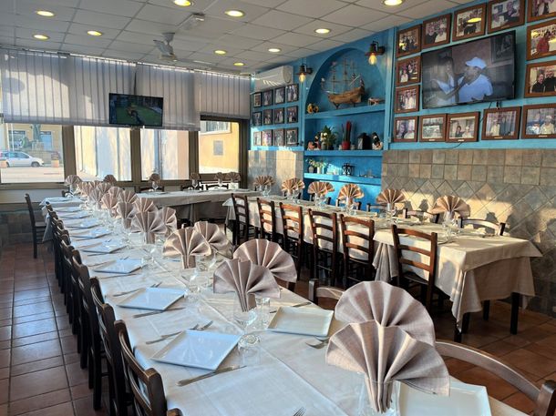 Lungo tavolo da pranzo di un ristorante con tovaglie bianche, tovaglioli piegati e decorazioni murali blu.