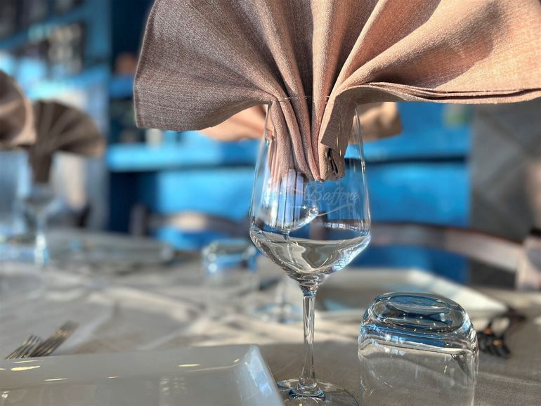 Elegante apparecchiatura della tavola con tovaglioli beige piegati nei calici da vino e uno sfondo sui toni del blu.