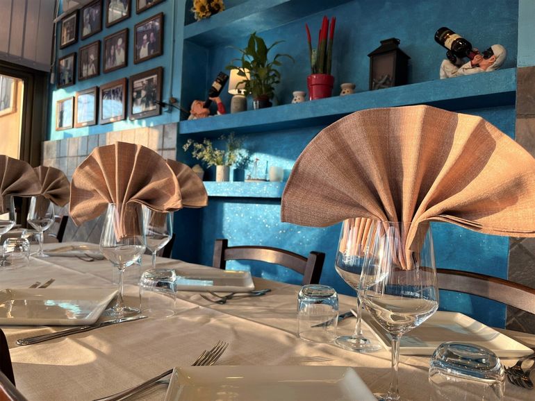 Tavolo apparecchiato con tovaglioli color rame in un interno di ristorante blu con scaffali e decorazioni