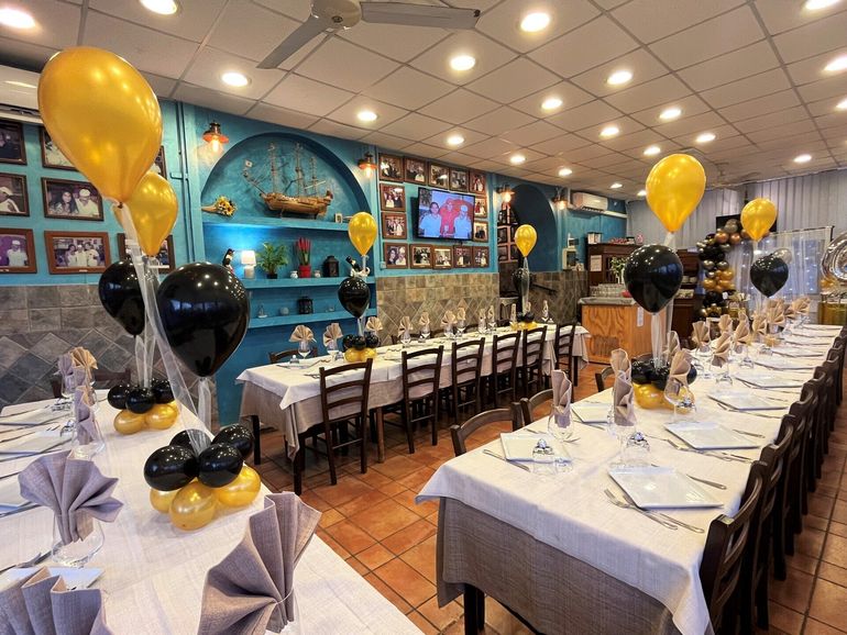 Sala per banchetti decorata con lunghi tavoli, palloncini neri e dorati e opere d'arte blu alle pareti.