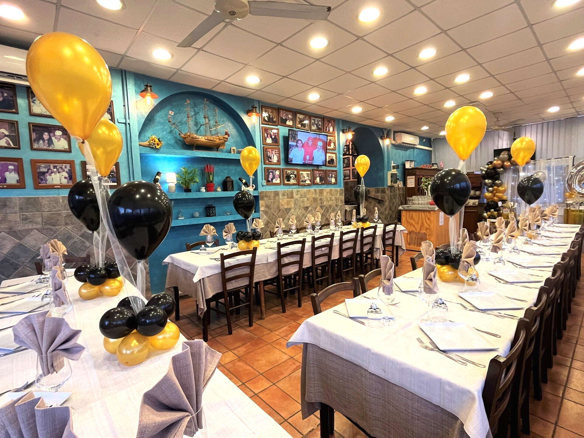 Sala da pranzo del ristorante decorata con lunghi tavoli, tovaglie bianche e palloncini neri e dorati.