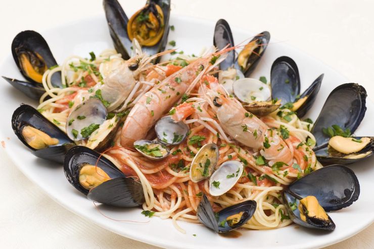 Pasta ai frutti di mare con cozze, gamberi ed erbe aromatiche su un piatto bianco.