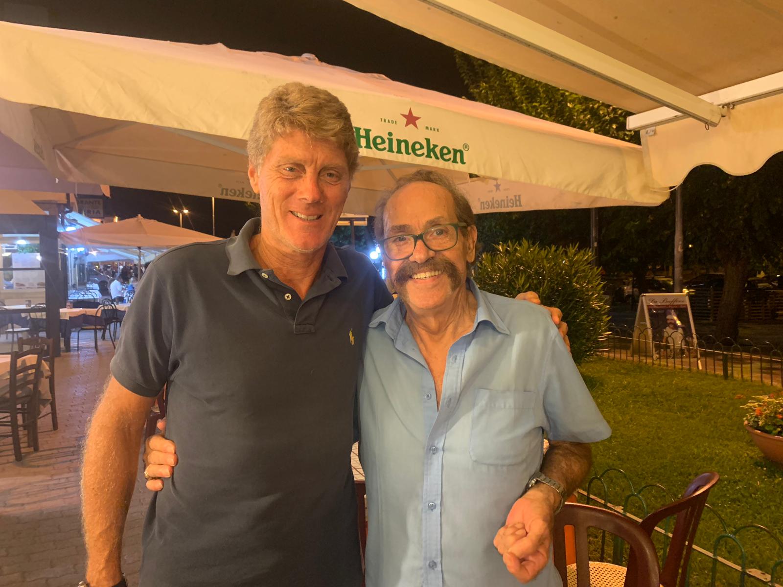 Due persone sorridenti in piedi insieme sotto un ombrellone Heineken in un patio all'aperto di notte.
