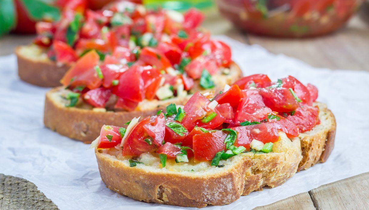 Bruschetta al pomodoro e basilico su fette di pane tostato adagiate su una superficie di marmo.