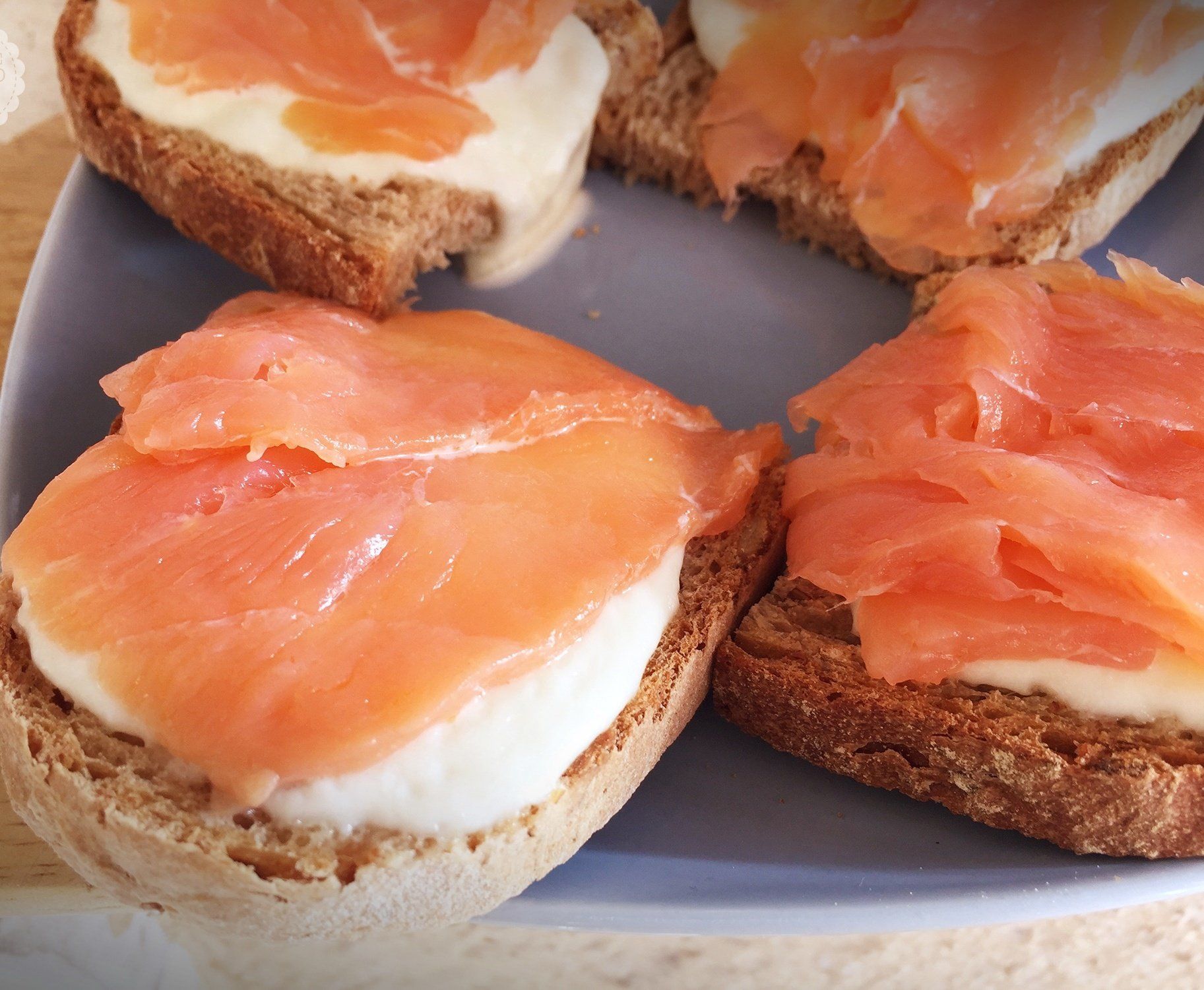 Tramezzini aperti con salmone affumicato e formaggio cremoso, serviti su un piatto bianco.