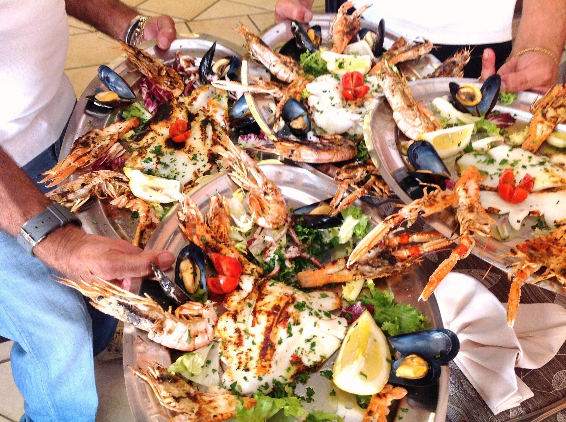 Mani che servono un grande piatto di frutti di mare con granchio, cozze, gamberi, limone ed erbe aromatiche su un tavolo