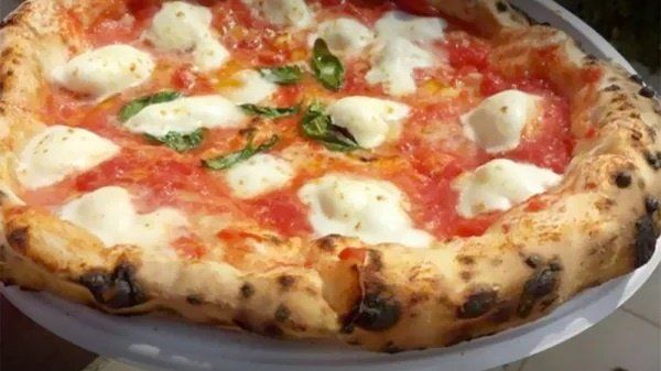 Primo piano di una pizza Margherita ricca di formaggio, con salsa di pomodoro e foglie di basilico, cotta in padella.