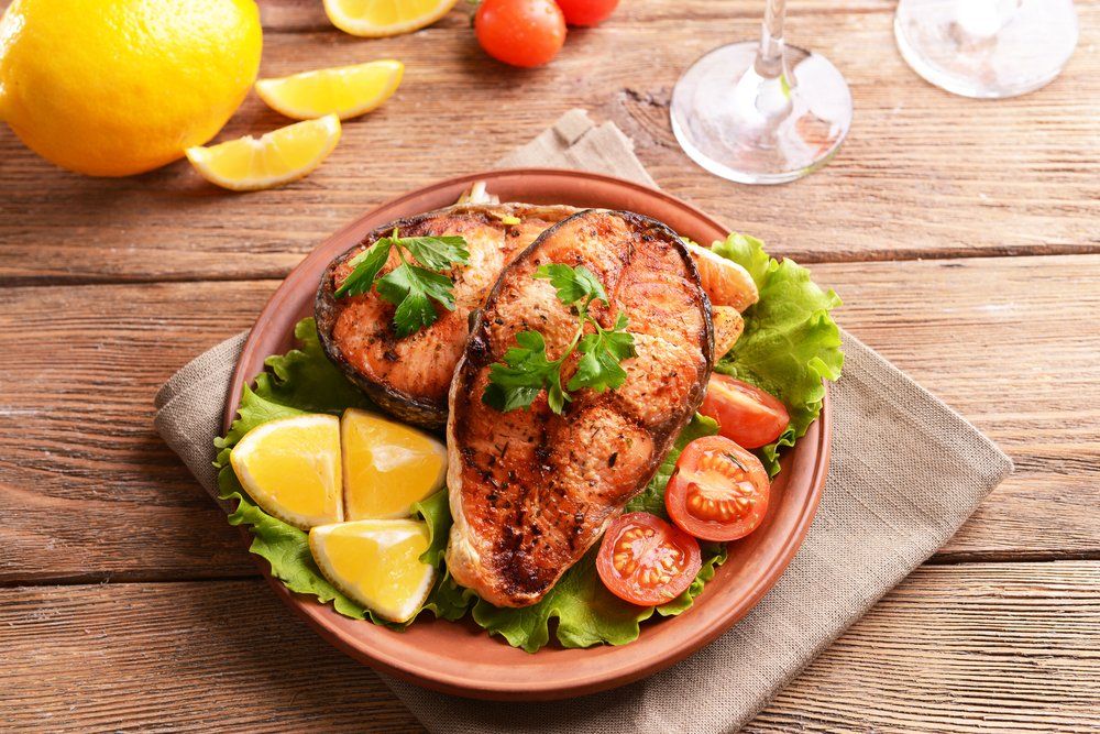 Petto di pollo grigliato con spicchi di lime, pomodorini e lattuga su un piatto marrone con tavolo di legno