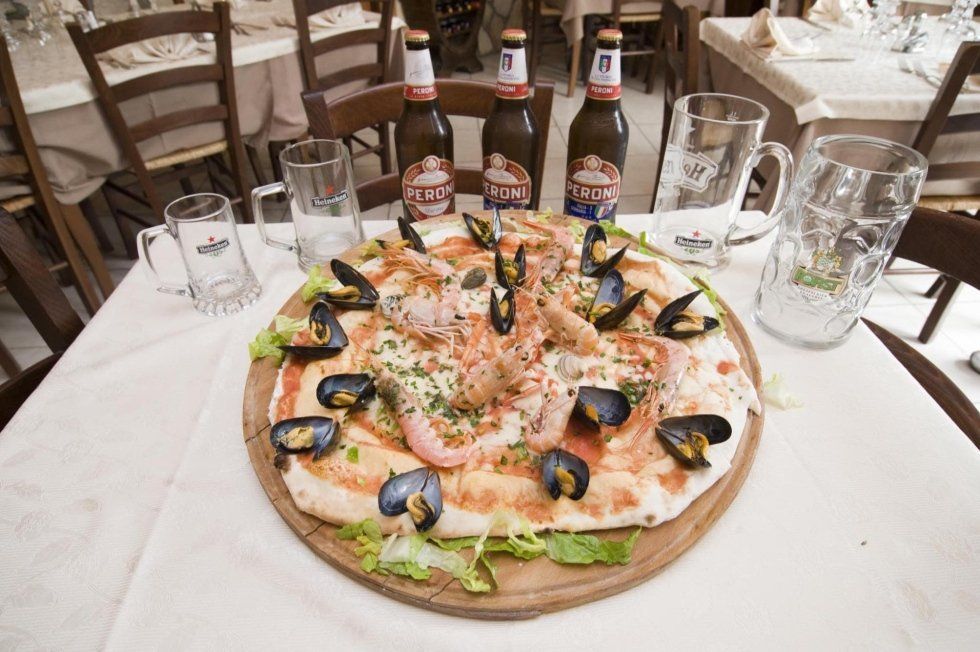 Pizza ai frutti di mare su un tavolo con bevande e bottiglie di birra in un ristorante