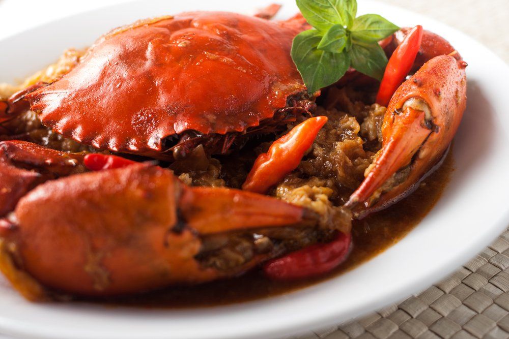 Granchio al vapore in salsa rossa lucida, servito su un piatto bianco e guarnito con foglie di basilico.
