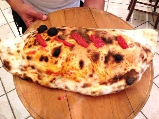 Calzone grande condito con pomodori e olive su un tagliere di legno per pizza.