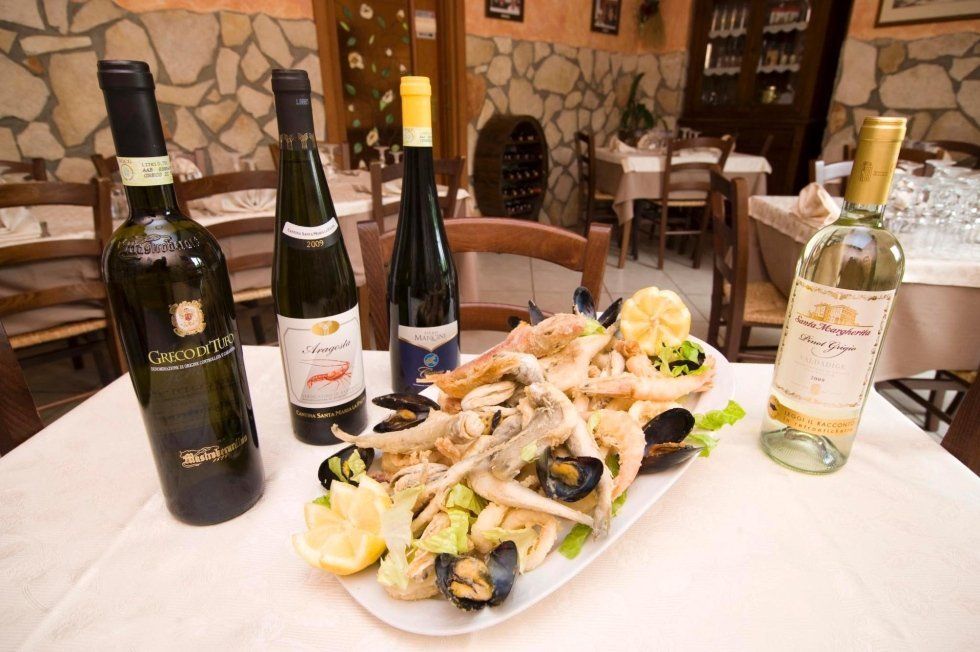 Bottiglie di vino e un piatto di frutti di mare su un tavolo in un ristorante rustico, con muri in pietra sullo sfondo.