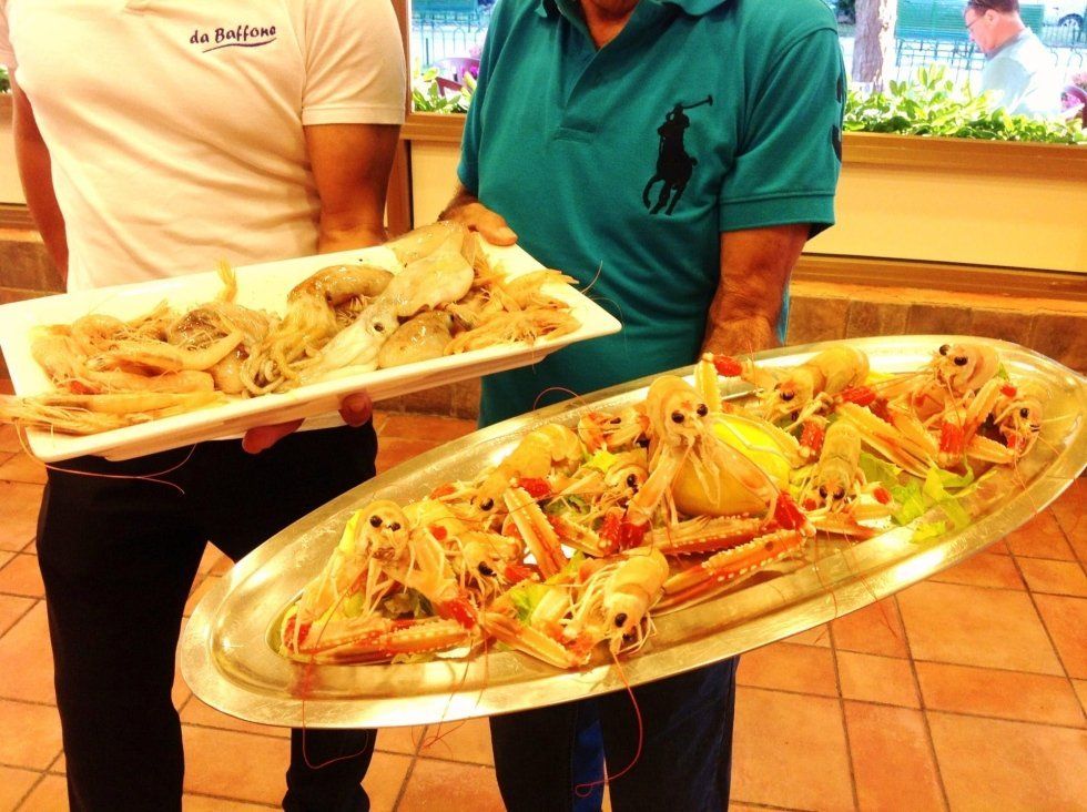 Due persone che reggono vassoi di cibo assortito in una luminosa mensa o area buffet.