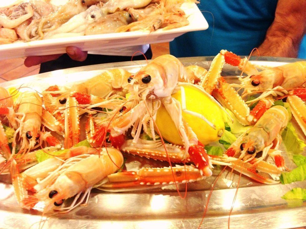 Piatto di zampe di granchio e gamberi cotti con spicchi di limone e salse, servito su un vassoio di metallo.