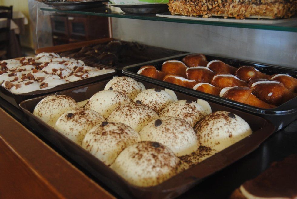 Un vassoio di panini appena sfornati e cosparsi di spezie su uno scaffale espositivo di una pasticceria, insieme ad altri prodotti di pasticceria.