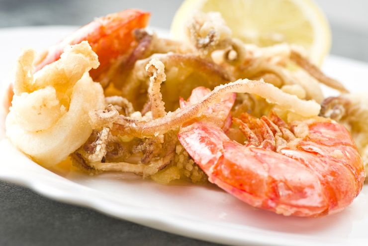 Frutti di mare fritti misti su un piatto bianco, tra cui gamberi e calamari, con uno spicchio di limone.