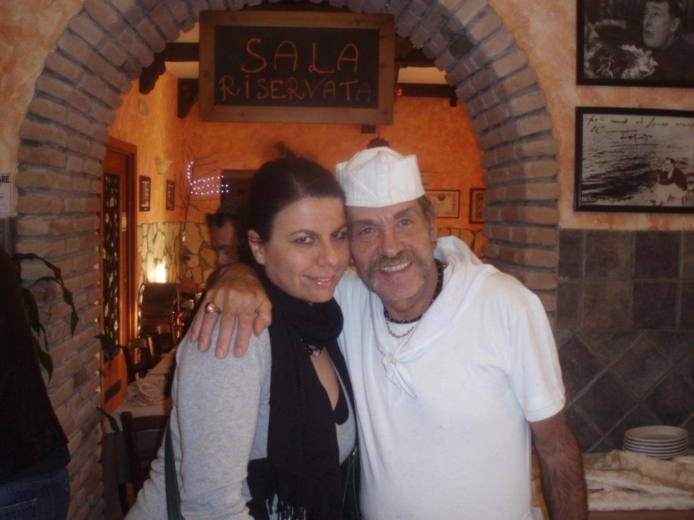 Due persone sorridenti posano insieme in un accogliente ristorante in mattoni con un portale ad arco.