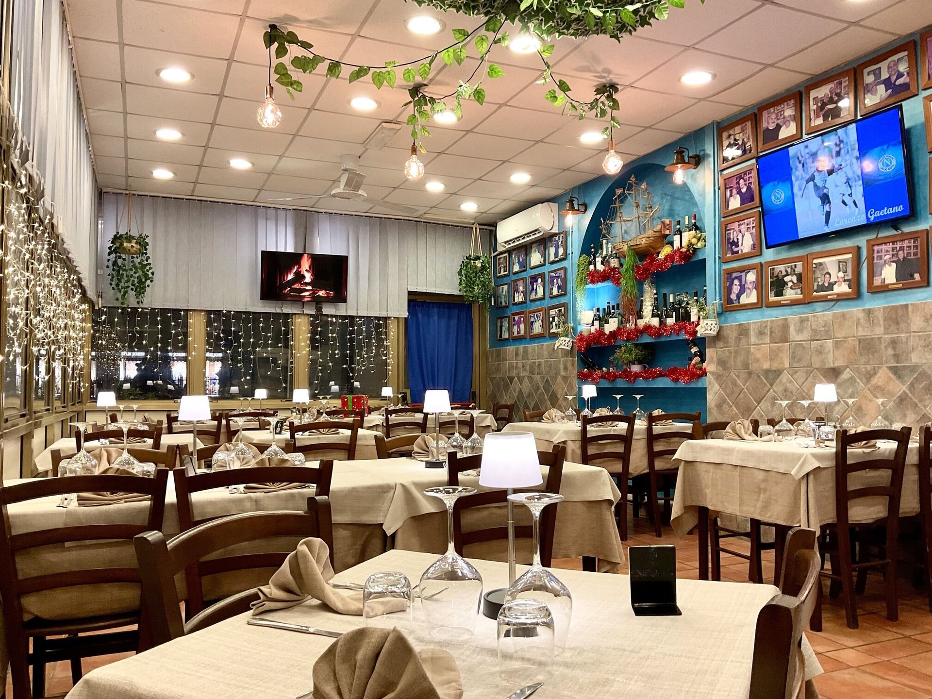 Sala da pranzo con tovaglie bianche, sedie in legno, lampade a sospensione e quadri colorati alle pareti.